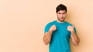 Bej arka planda izole edilmiş genç adam parmağını göstererek şaşırdı, geniş bir gülümsemeyle..