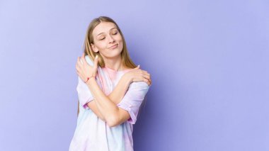 Genç sarışın kadın, mor arka planda izole edilmiş. Kucaklaşma, kaygısız gülümseme ve mutluluk..