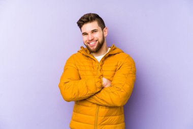 Mor arka planda izole genç bir adam kendinden emin, kararlılıkla kollarını kavuşturuyor..