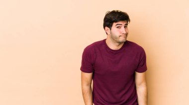 Bej arka planda izole edilmiş genç adam omuz silkiyor ve gözleri açık..