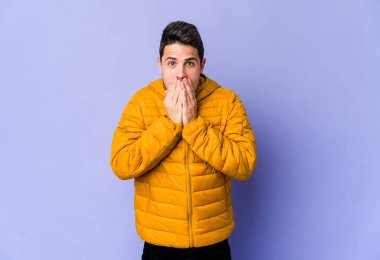 Mor arka planda izole edilmiş genç beyaz adam elleriyle ağzını kapatırken şok oldu..