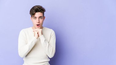 Kafkasyalı genç adam mor arka planda izole edilmiş şans diliyor, şaşırmış ve ağzı açık bir şekilde önüne bakıyor..