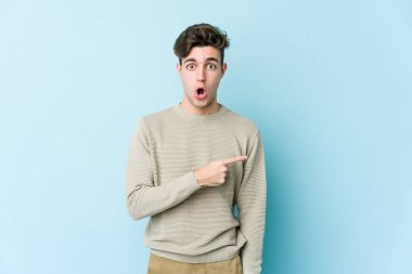 Mavi arka planda izole edilmiş genç beyaz adam yan tarafı işaret ediyor.