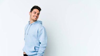 Beyaz arka planda izole edilmiş genç beyaz adam gülümseyen, neşeli ve keyifli bir tarafa bakıyor..