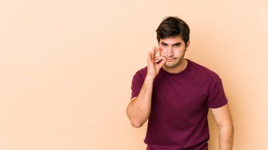 Bej arka planda izole edilmiş genç bir adam, parmakları dudaklarında bir sır saklıyor..