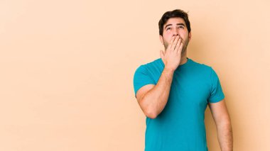 Bej arka planda izole edilmiş genç bir adam esniyor. Ağzı eliyle kapatan yorgun bir jest gösteriyor..