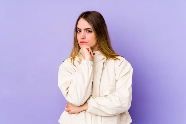 Young caucasian woman isolated on purple background suspicious, uncertain, examining you.