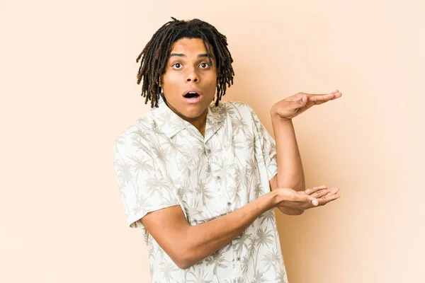 Young african american rasta man shocked and amazed holding a copy space between hands.