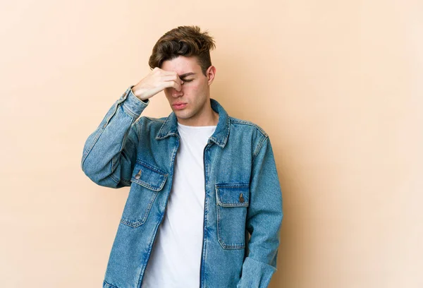 Young caucasian man isolated on beige background having a head ache, touching front of the face.