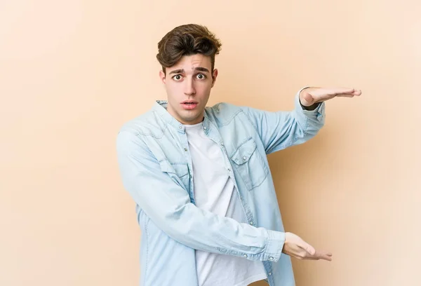 Young Caucasian Man Isolated Beige Background Shocked Amazed Holding Copy — Stock Photo, Image