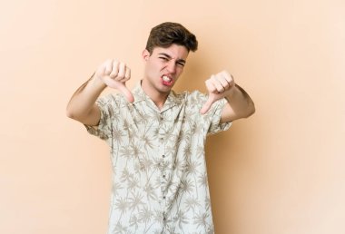Beyazların arka planında izole edilmiş genç beyaz bir adam baş parmağını aşağı gösteriyor ve hoşlanmadığını ifade ediyor..