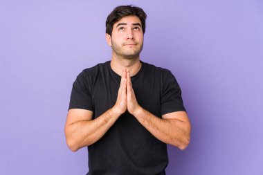 Mor arka planda izole olmuş genç bir adam. El ele tutuşup, ağzının kenarında dua ediyor. Kendine güveniyor..