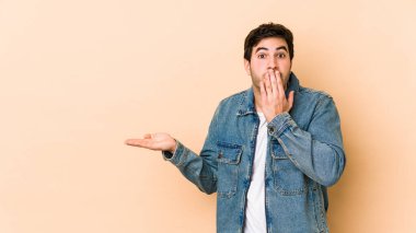 Bej arka planda izole edilmiş genç adam, avuç içinde kopya alanı tutmaktan etkilenmiş..