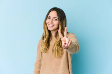 Mavi arka planda izole edilmiş genç beyaz kadın iki numarayı parmaklarıyla gösteriyor..