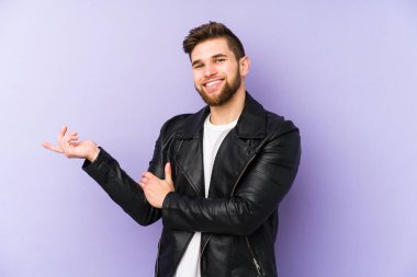 Mor arka planda izole edilmiş genç adam işaret parmağıyla işaret ederek gülümsüyor..