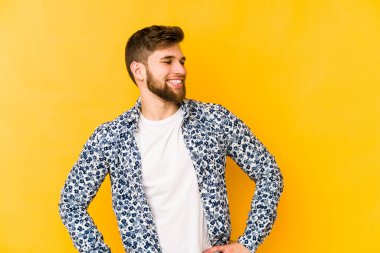 Sarı arka planda izole edilmiş genç beyaz adam ellerini kalçalarına koyuyor..