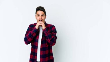 Beyaz arka planda izole edilmiş genç beyaz bir adam şans için dua ediyor, şaşırmış ve ağzını açıp önüne bakıyor..