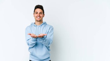 Beyaz arka planda izole edilmiş genç beyaz bir adam elinde avuç içi bir şeyle kameraya sunuyor..