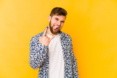 Sarı arka planda izole edilmiş genç beyaz adam parmaklarıyla kaya hareketi gösteriyor.