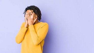 Rasta saç stili giyen genç siyahi adam parmaklarının arasından korkmuş ve gergin bir şekilde göz kırpıyor..