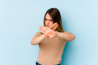 Mavi arka planda izole edilmiş genç beyaz bir kadın inkar jesti yapıyor.