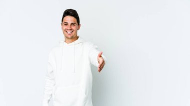 Beyaz arka planda izole edilmiş genç beyaz bir adam selamlama jesti olarak kameraya elini uzatıyor..