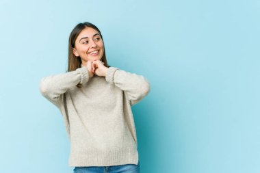 Genç beyaz kadın ellerini çenesinin altında tutuyor, mutlu bir şekilde yan tarafa bakıyor..