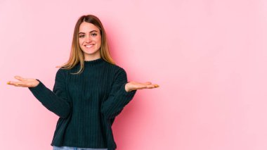 Pembe arka planda izole edilmiş genç beyaz kadın kollarıyla ölçek oluşturuyor, mutlu ve kendinden emin hissediyor..