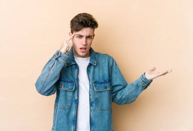 Beyazlı genç bir adam bej arka planda izole edilmiş ve elinde bir ürün var..