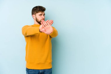 Mavi arka planda izole edilmiş genç beyaz adam elini uzatmış, dur işareti göstererek seni engelliyor..