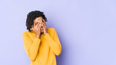 Rasta saç stili giyen genç siyahi adam kameraya parmaklarıyla göz kırpıyor, yüzünü kapatmaktan utanıyor..