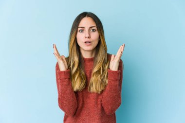 Mavi arka planda izole edilmiş genç beyaz kadın şaşırdı ve şok oldu..