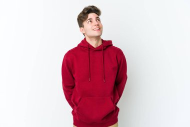 Beyaz arka planda izole edilmiş genç beyaz adam gevşemiş ve mutlu bir şekilde gülüyor, boynunda dişlerini gösteriyor..