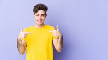 Mor arka planda izole genç beyaz adam parmaklarıyla aşağı noktalar, olumlu duygu.