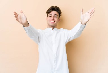 Beyazlı genç adam bej arka planda izole edilmiş kameraya sarıldığı için kendinden emin hissediyor..