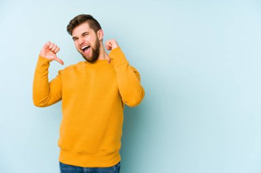 Mavi arka planda izole edilmiş genç beyaz adam gururlu ve kendinden emin hissediyor, örnek olarak.