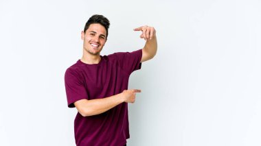 Beyaz arka planda izole edilmiş genç beyaz bir adam işaret parmaklarıyla küçük bir şey tutuyor, gülümsüyor ve kendinden emin..