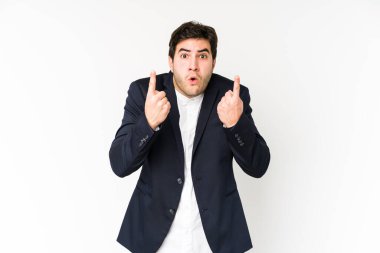 Beyaz arka planda izole edilmiş genç iş adamı ağzı açık bir şekilde üst tarafı işaret ediyor..