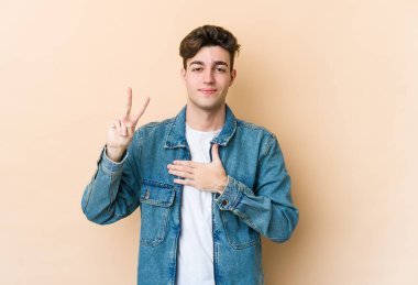 Beyaz tenli genç adam bej arka planda izole edilmiş yemin ediyor, elini göğsüne koyuyor..