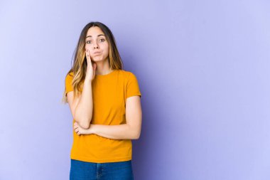 Mor arka planda izole edilmiş genç beyaz kadın yanakları patlatıyor, yorgun bir ifadesi var. Yüz ifadesi kavramı.