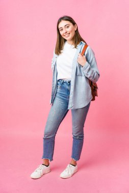 Pembe arka planda tek başına okula giden genç bir kız öğrenci.