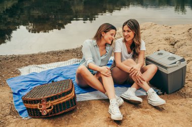 İki genç kız arkadaş doğadaki bir gölün ortasında piknik yapıyorlar..