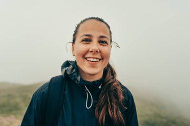 Yürüyüşçü bulutlu bir günde dağın tepesinde doğanın ortasında gülümsüyor..