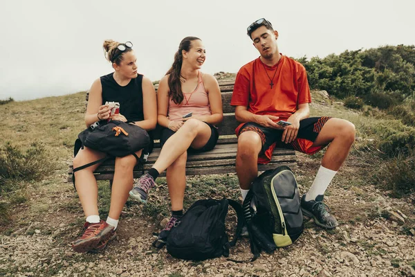 Hikers sitting on a bench on top of a mountain resting and smiling.