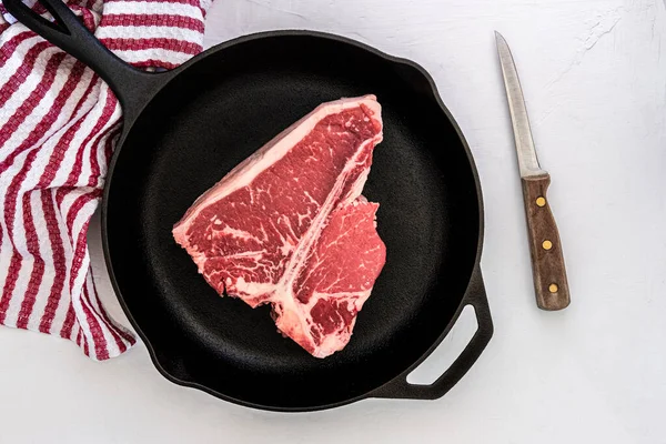 Photograph of a T-Bone choice cut steak in a cast iron skillet with a boning knife and towel in background
