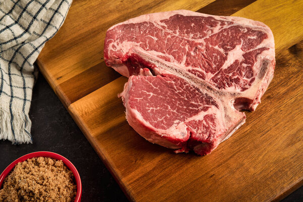 Photograph of Porterhouse steak on a cutting board, with a spicy brown suger rub on the side, with a kitchen towel in the background