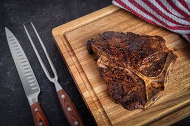Taze pişmiş biftek, tahta kesme tahtasının üzerinde bir bıçak ve çatal oyma setiyle dinleniyor.