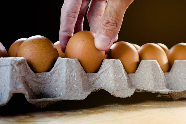 Человек держит свежее куриное яйцо в бумажной панели на деревянном столе
