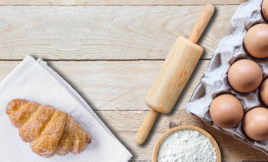 Beyaz kumaşta taze kruvasan ve kağıt panelde yumurta. Kase içinde un olan yuvarlanan bir iğne. Kopya alanı olan ahşap tablo