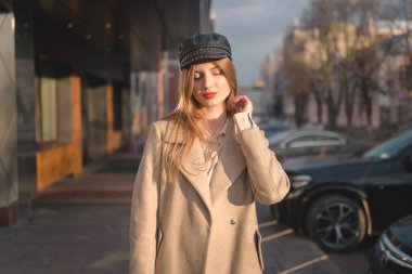 Şehir Yürüyüşü 'ndeki Şık Giyimli Kadın Portresi. Şehirde çekilen güzel bir kızla fotoşop. Profesyonel fotoşop: Paltolu ve şapkalı güzel bir kadın bahar (veya sonbahar) şehir sokaklarında yürüyor.